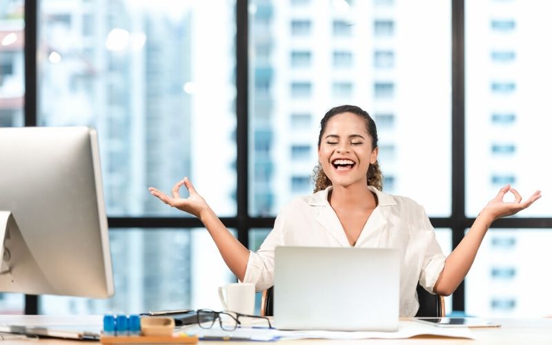 Happy business woman sitting behind her desk at work meditating in front of her computer