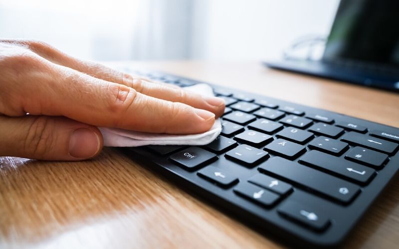 Wiping down keyboard with disinfectant wipe