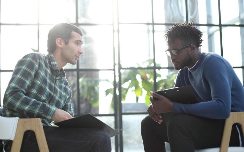 two men sitting in chairs with clipboards talking to each other