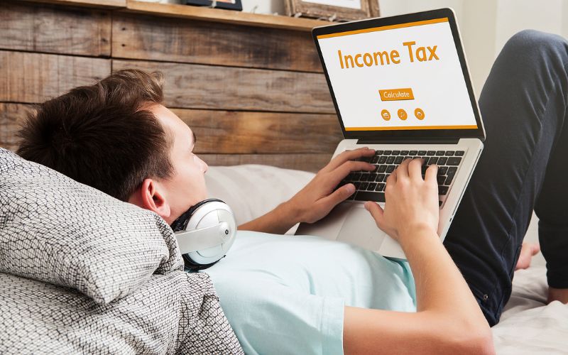 Man laying in bed doing taxes on his laptop