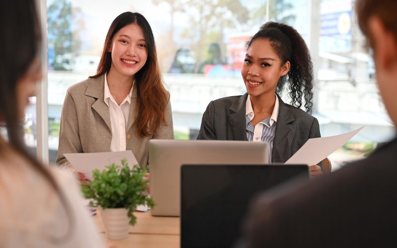 Two business women smiling in a meeting with a laptop in front of them.